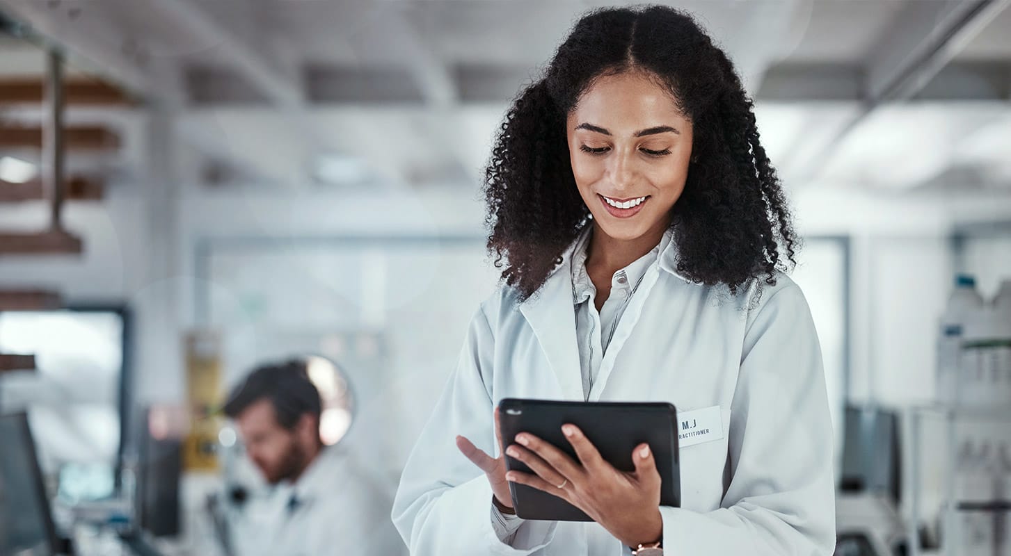 A woman wearing a lab coat is holding a tablet, appearing attentive and ready to analyze data.